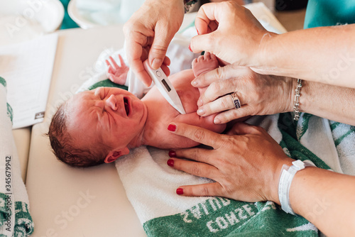 Nurses check a newborn baby on the hospital table. They take his temperature with a thermometer.