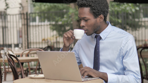 African Businessman Working on Laptop and Drinking Coffee in Outdoor Cafe