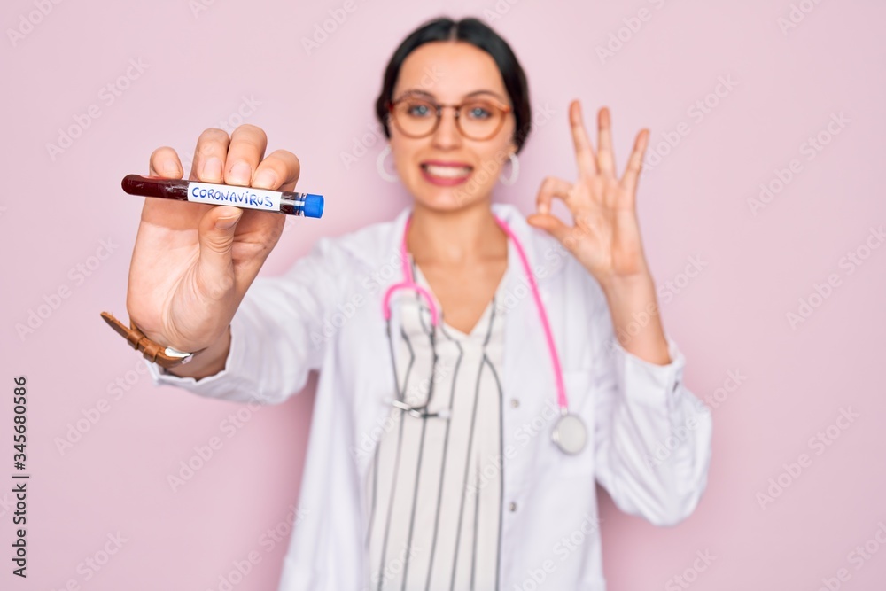 Beautiful doctor woman with blue eyes wearing stethoscope holding coronavirus test tube doing ok sign with fingers, excellent symbol Beautiful doctor woman with blue eyes wearing stethoscope holding coronavirus test tube doing ok sign with fingers, excellent symbol