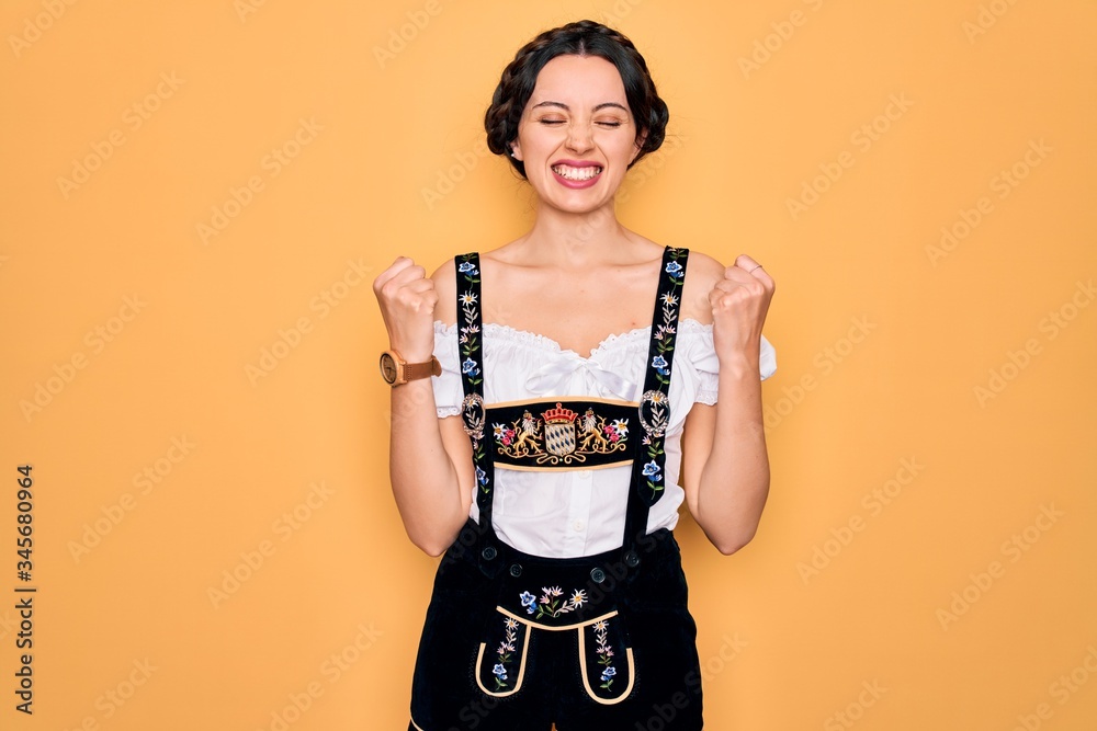 Young beautiful german woman with blue eyes wearing traditional octoberfest dress very happy and excited doing winner gesture with arms raised, smiling and screaming for success. Celebration concept. Young beautiful german woman with blue eyes wearing traditional octoberfest dress very happy and excited doing winner gesture with arms raised, smiling and screaming for success. Celebration concept.