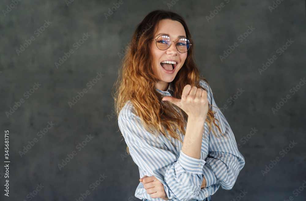 Image of happy attractive woman smiling and pointing thumb aside Image of happy attractive woman smiling and pointing thumb aside