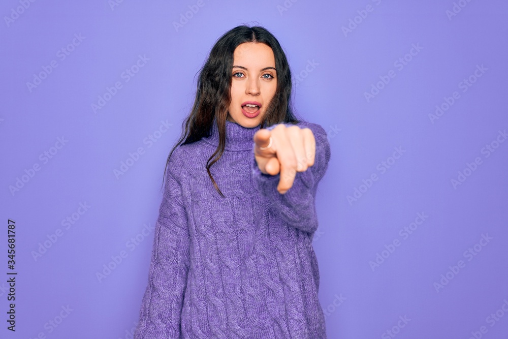 Young beautiful woman wearing casual turtleneck sweater standing over purple background pointing displeased and frustrated to the camera, angry and furious with you Young beautiful woman wearing casual turtleneck sweater standing over purple background pointing displeased and frustrated to the camera, angry and furious with you