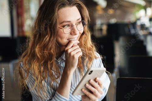 Image of cheerful young woman smiling and typing on cellphone