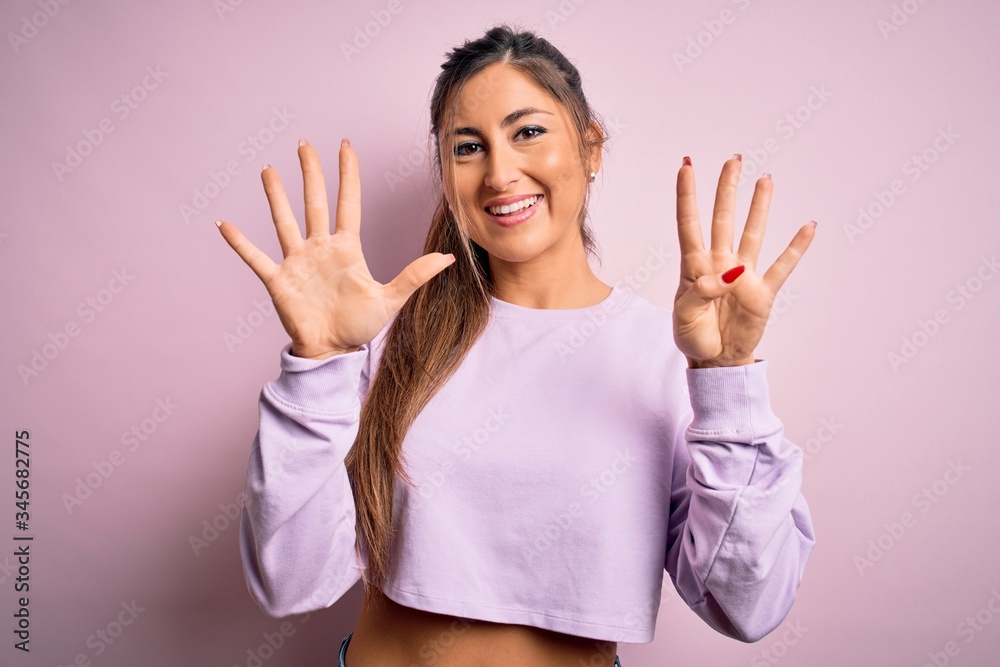 Young beautiful sport woman wearing sweatshirt over pink isolated background showing and pointing up with fingers number nine while smiling confident and happy. Young beautiful sport woman wearing sweatshirt over pink isolated background showing and pointing up with fingers number nine while smiling confident and happy.