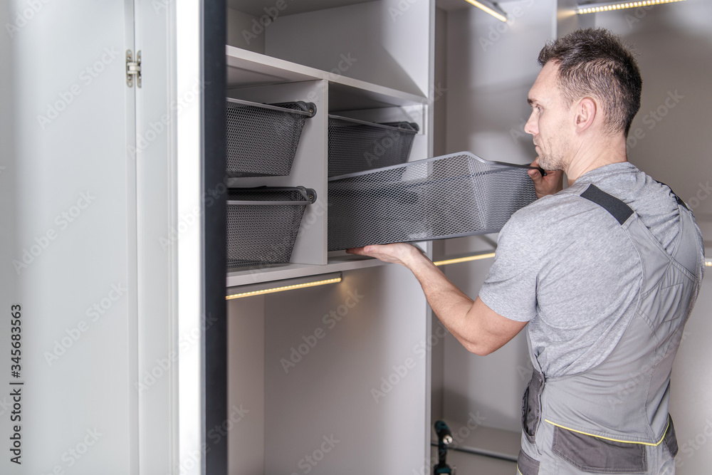 Male Handyman Finishes Installation Of Walk In Closet And Storage Area. Male Handyman Finishes Installation Of Walk In Closet And Storage Area.