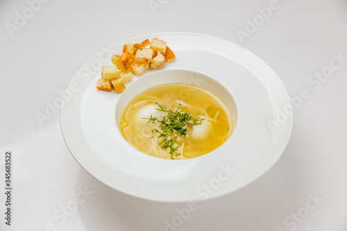 A white plate of soup with noodles, quail eggs and croutons