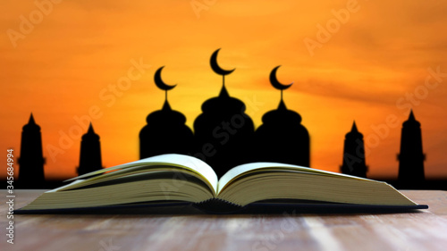 open book on wood table with silhouette mosque i sun set or sun rise beautiful background.the quran open on table for muslim people prayer in namaz time.