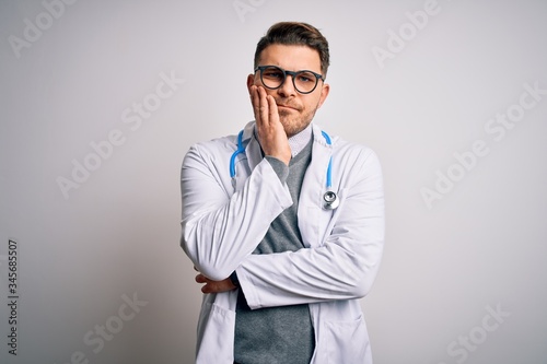 Young doctor man with blue eyes wearing medical coat and stethoscope over isolated background thinking looking tired and bored with depression problems with crossed arms. © Krakenimages.com