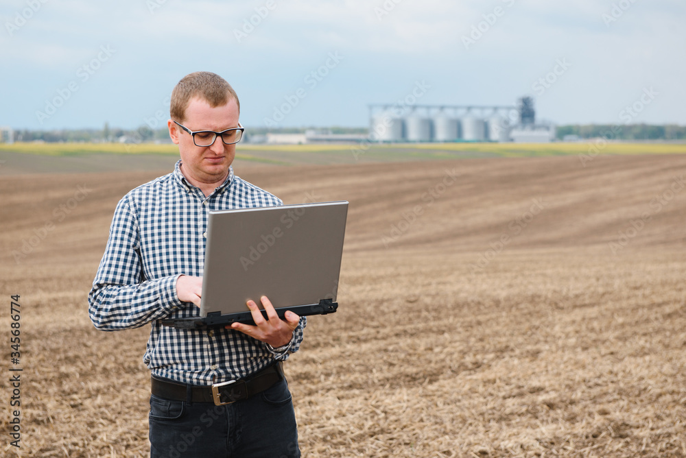 Happy farmer with laptop standing in wheat field in front of grain silo Happy farmer with laptop standing in wheat field in front of grain silo
