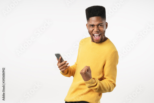 Portrait of excited young man with mobile phone isolated over white background and celebrating © InsideCreativeHouse