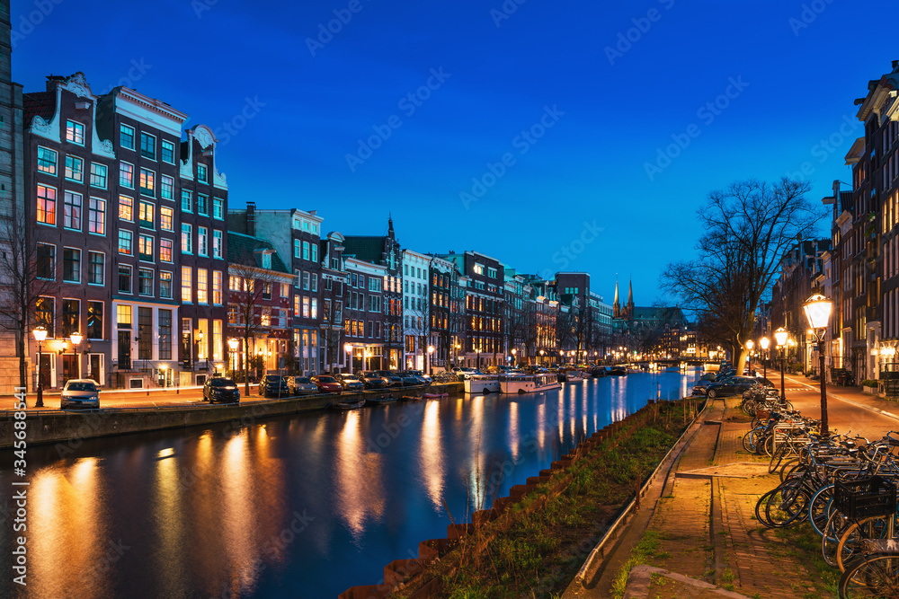 Amsterdam canal with typical dutch dancing houses at night with city lights reflections in water, Holland, Netherlands.
