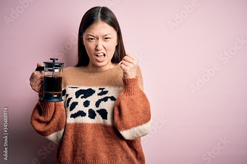 Young asian woman making a glass of coffe using french press coffee maker over pink background annoyed and frustrated shouting with anger  crazy and yelling with raised hand  anger concept