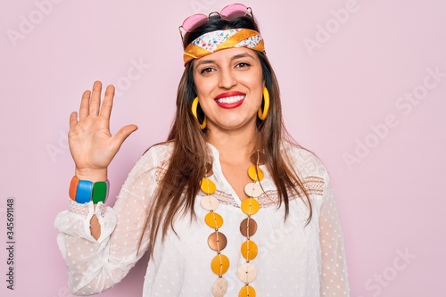 Young hispanic hippie woman wearing fashion boho style and sunglasses over pink background showing and pointing up with fingers number five while smiling confident and happy.