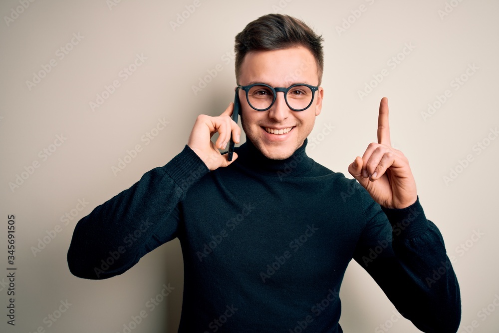 Young handsome caucasian man having a conversation talking on smartphone surprised with an idea or question pointing finger with happy face, number one Young handsome caucasian man having a conversation talking on smartphone surprised with an idea or question pointing finger with happy face, number one