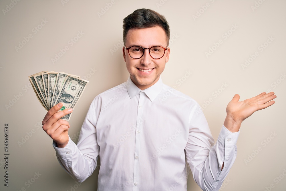 Young handsome caucasian business man holding bunch of one dollar banknotes very happy and excited, winner expression celebrating victory screaming with big smile and raised hands Young handsome caucasian business man holding bunch of one dollar banknotes very happy and excited, winner expression celebrating victory screaming with big smile and raised hands