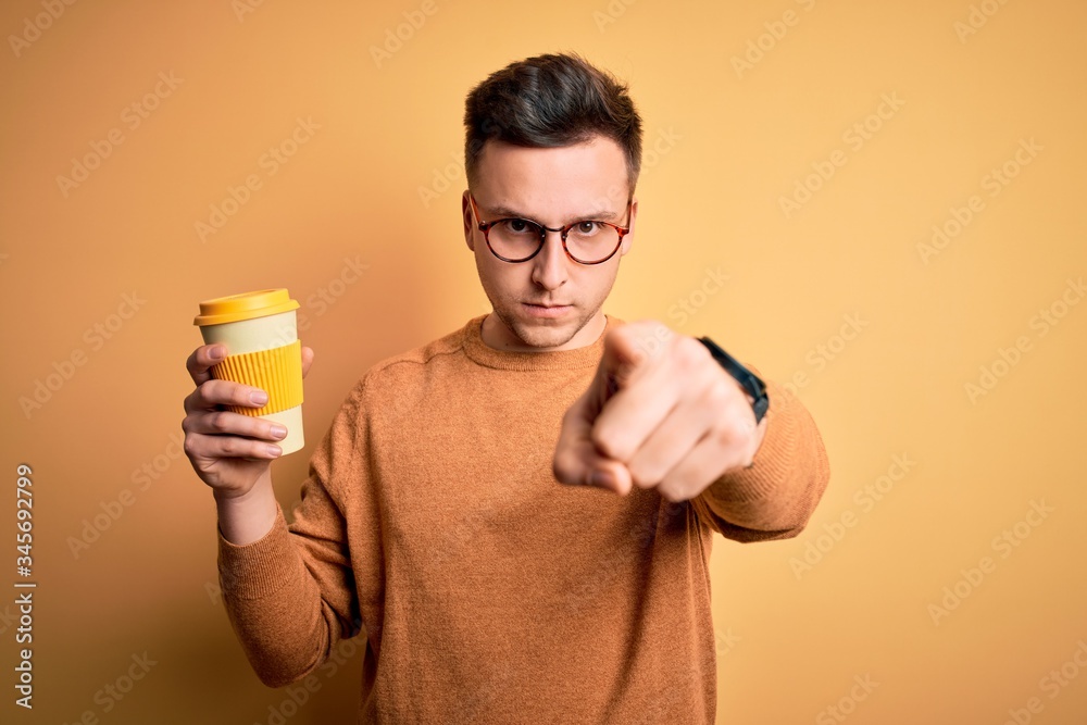 Young handsome caucasian man drinking coffee from a take away thermo bottle pointing with finger to the camera and to you, hand sign, positive and confident gesture from the front Young handsome caucasian man drinking coffee from a take away thermo bottle pointing with finger to the camera and to you, hand sign, positive and confident gesture from the front