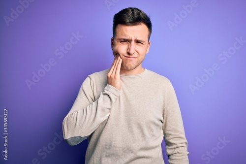 Young handsome caucasian man wearing casual sweater over purple isolated background touching mouth with hand with painful expression because of toothache or dental illness on teeth. Dentist