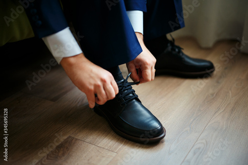 Man tying the laces on black shoes on a wooden floor.