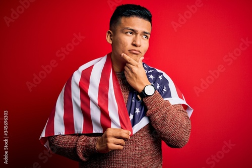 Young handsome latin patriotic man wearing united states of america falg serious face thinking about question, very confused idea photo