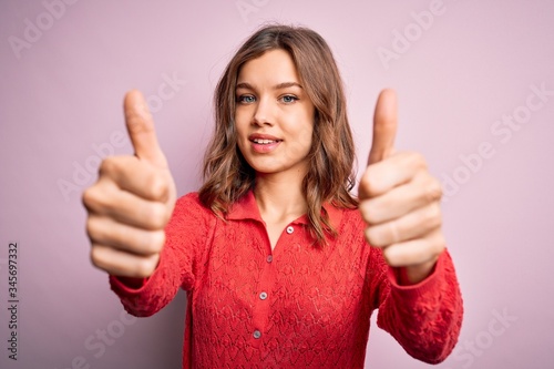 Young beautiful blonde casual girl over pink isolated background approving doing positive gesture with hand, thumbs up smiling and happy for success. Winner gesture. © Krakenimages.com