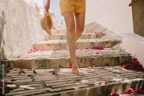 legs of a girl in a summer dress barefoot with a straw hat in the Mediterranean in a village on stone paved steps