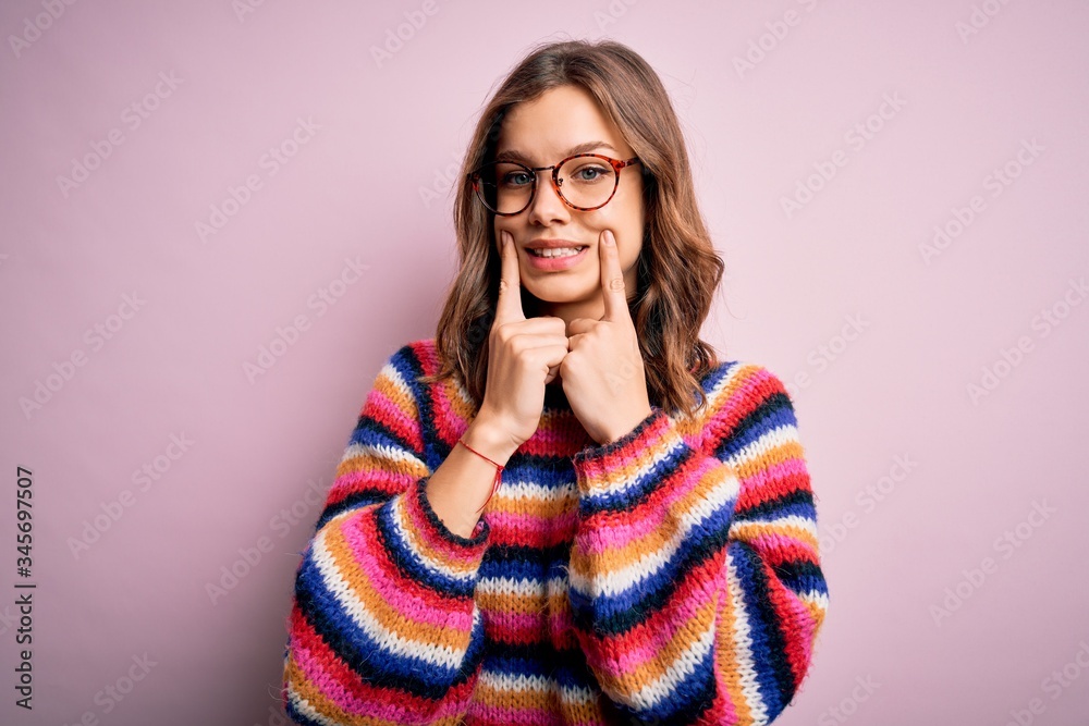 Young beautiful blonde girl wearing glasses and casual sweater over pink isolated background Smiling with open mouth, fingers pointing and forcing cheerful smile
