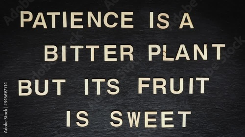 Stop motion of wooden letters writing PATIENCE IS A BITTER PLANT on slate background