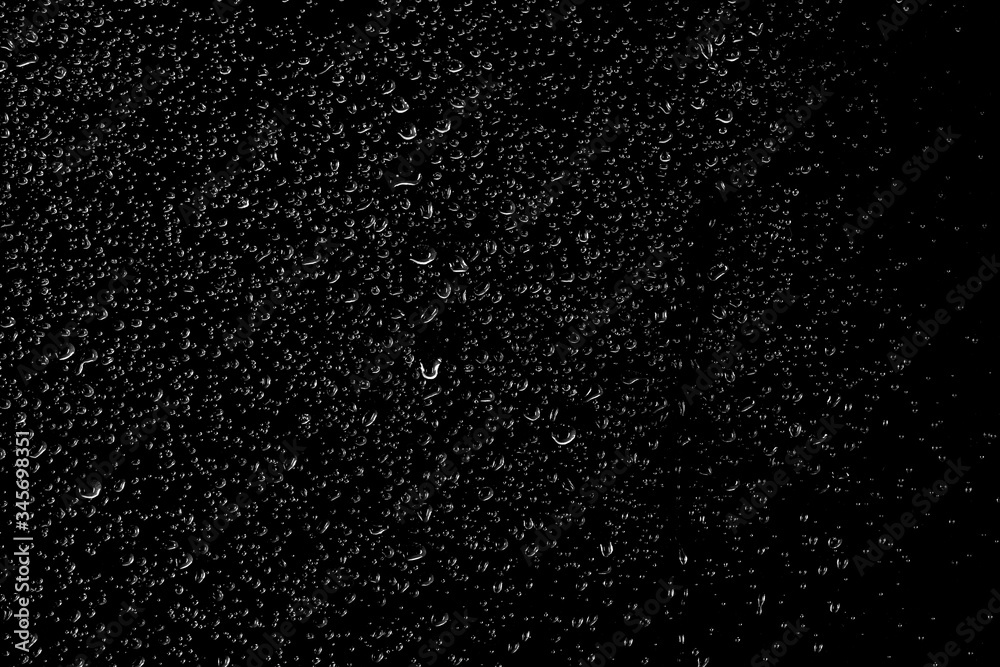 Obraz premium Drops of water flow down the surface of the clear glass on a black background. 