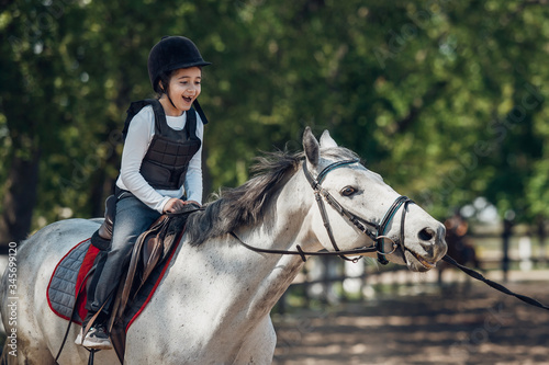 Smiling Little Girl in helmet Learning Horseback Riding. Instructor teaches kid Equestrian. © sergiophoto