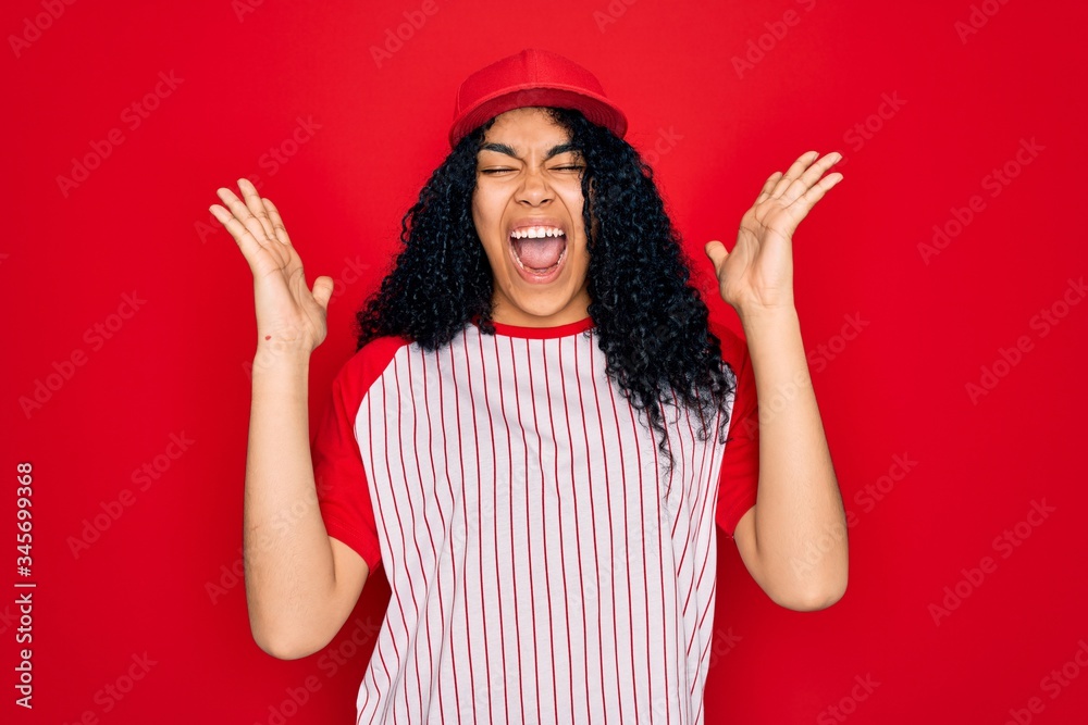 Young african american curly sportswoman wearing baseball cap and striped t-shirt celebrating mad and crazy for success with arms raised and closed eyes screaming excited. Winner concept Young african american curly sportswoman wearing baseball cap and striped t-shirt celebrating mad and crazy for success with arms raised and closed eyes screaming excited. Winner concept