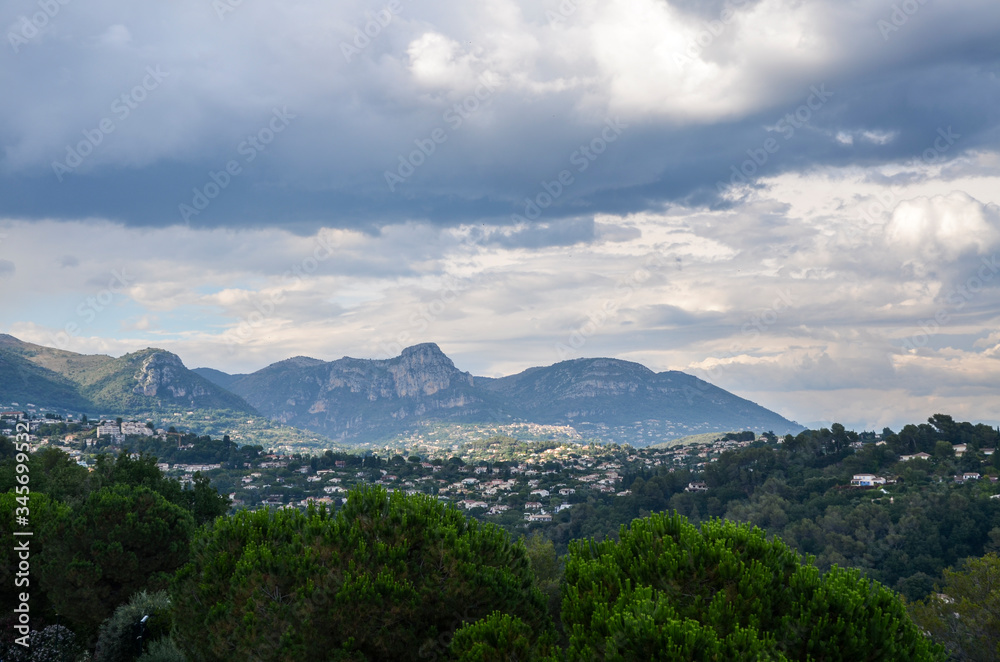 Panoramic rural landscape of hills with the Maritime Alps mountains in the distance near the village Saint-Paul-de-Vence,  Provence region, southeastern France at sunny summer day