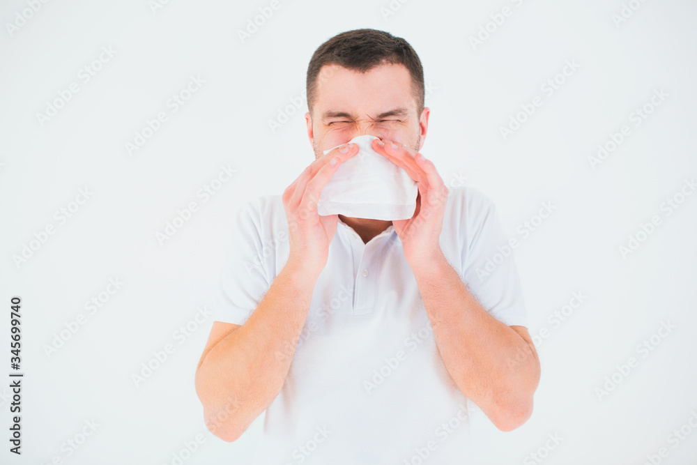 Young man isolated over white background. Cover nose with white tissue. Sick and ill person sneezing into white napkin. Coronavirust symptoms. Young man isolated over white background. Cover nose with white tissue. Sick and ill person sneezing into white napkin. Coronavirust symptoms.