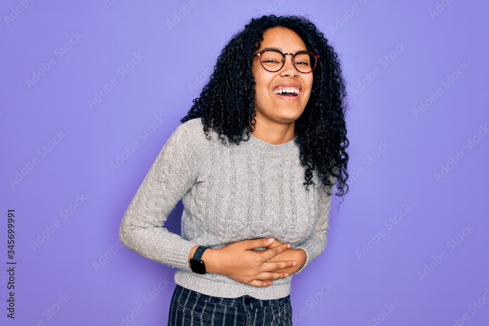 Young african american woman wearing casual sweater and glasses over purple background smiling and laughing hard out loud because funny crazy joke with hands on body. Young african american woman wearing casual sweater and glasses over purple background smiling and laughing hard out loud because funny crazy joke with hands on body.