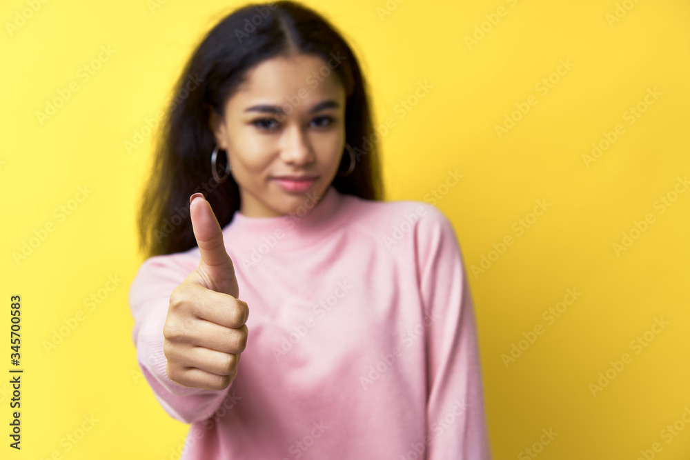 Happy smiling black woman showing thumbs up on yellow background. Focus on hand Happy smiling black woman showing thumbs up on yellow background. Focus on hand
