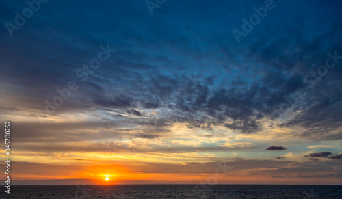 Sunset and dramatic set of clouds drifting over the tropical waters of the Caribbean Sea are lit by the last moments of daylight.