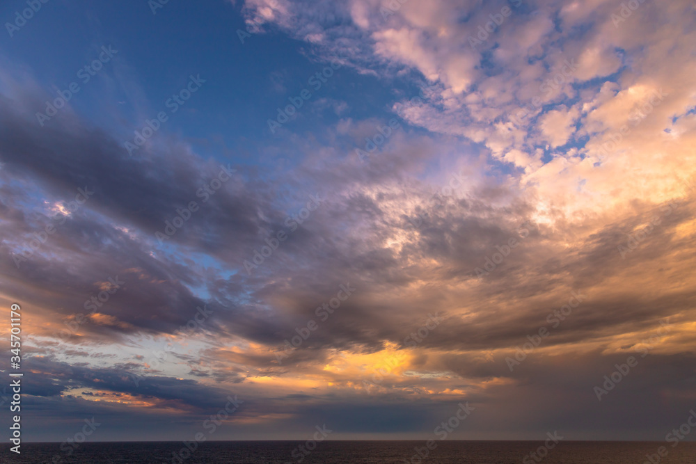 Sunset and dramatic set of clouds drifting over the tropical waters of the Caribbean Sea are lit by the last moments of daylight.