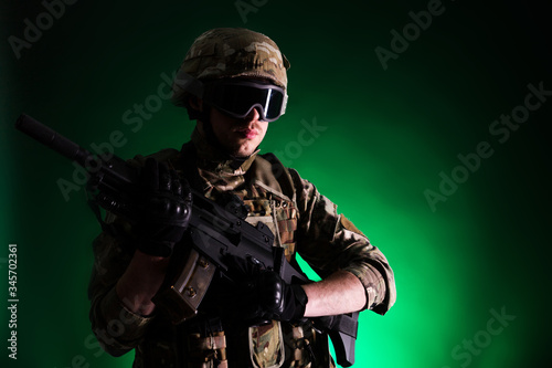 Soldier with gun is on mission on green background. Concept of war. photo