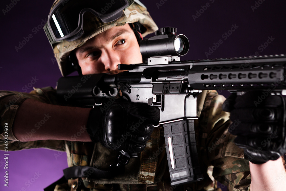 Soldier with gun is looking through the scope on violet background. Concept of war. Veterans, comrades, soldiers. Man in uniform. Soldier with gun is looking through the scope on violet background. Concept of war. Veterans, comrades, soldiers. Man in uniform.