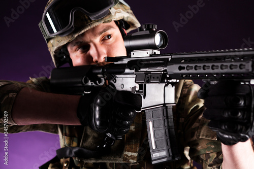 Soldier with gun is looking through the scope on violet background. Concept of war. Veterans, comrades, soldiers. Man in uniform.