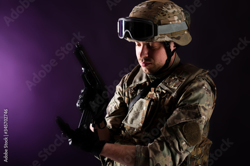 Soldier reloads gun on mission on violet background. Concept of war. photo