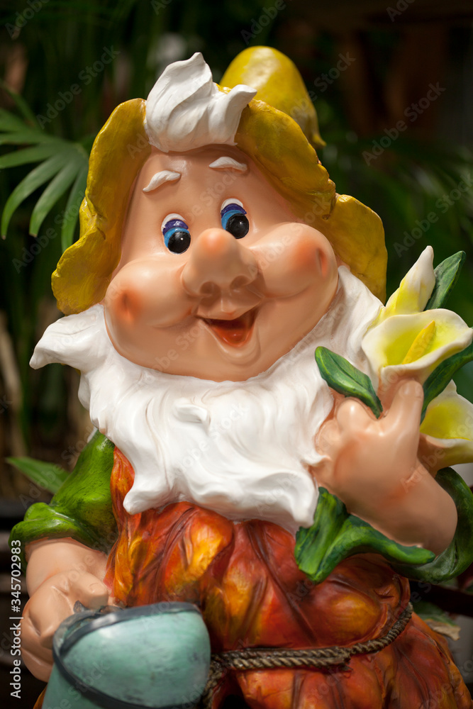 Cute dwarf living in a garden. Smiling garden gnome decoration against a blurry background. Funny elf in the garden. Happy dwarf figurine.