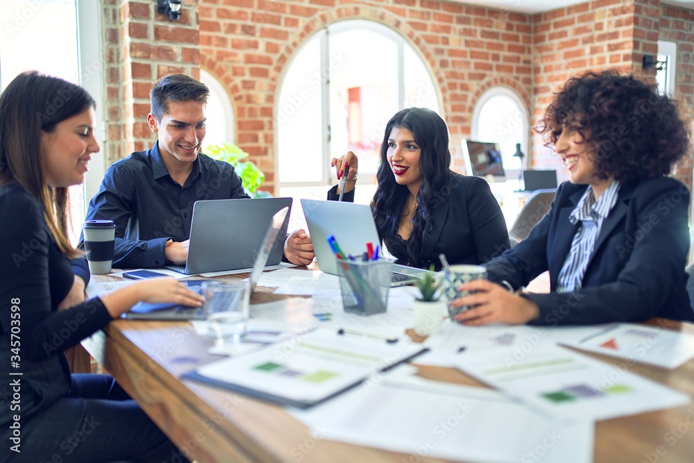 Group of business workers smiling happy and confident. Working together with smile on face using laptop and speaking at the office Group of business workers smiling happy and confident. Working together with smile on face using laptop and speaking at the office