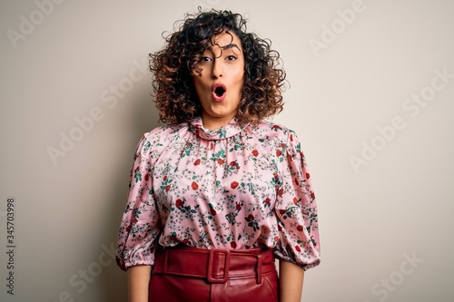 Young beautiful curly arab woman wearing floral t-shirt standing over isolated white background afraid and shocked with surprise expression, fear and excited face.