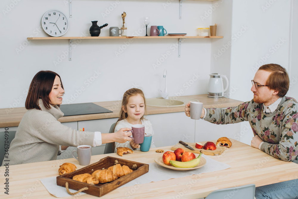 Young happy family with two kids having breakfast together. redheaded dad, kids and brunette mom together in the kitchen. Young happy family with two kids having breakfast together. redheaded dad, kids and brunette mom together in the kitchen.