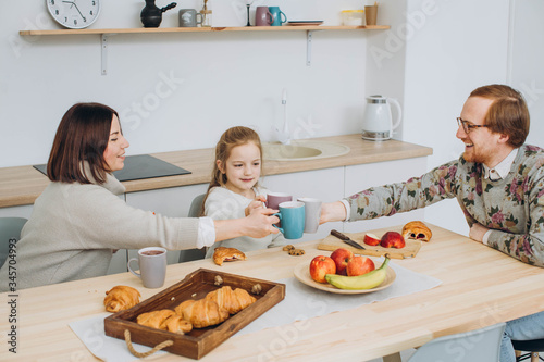 Young happy family with two kids having breakfast together. redheaded dad, kids and brunette mom together in the kitchen.