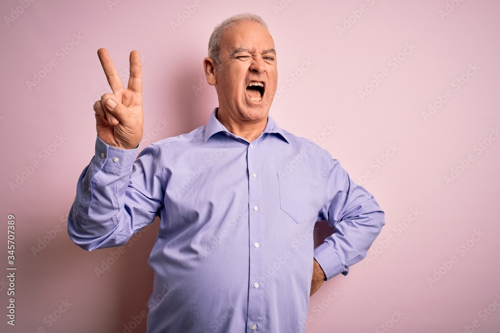 Fototapeta premium Middle age handsome hoary man wearing casual shirt standing over pink background smiling with happy face winking at the camera doing victory sign. Number two.