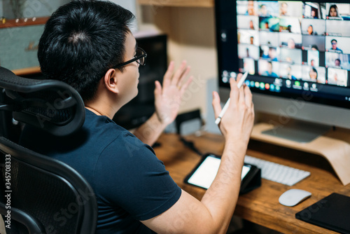 Young asian business man using computer for a online business meeting with his colleagues about plan in video conference. back view of business man have webcam group conference with coworkers at home