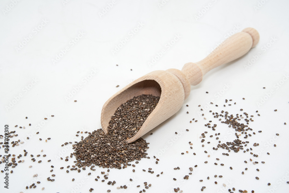 Mini wooden kitchen shovel with scattered chia seeds isolated on white background