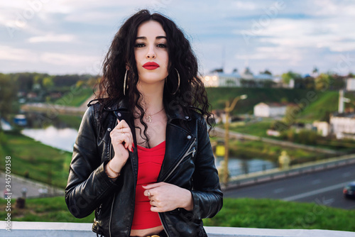 Fashion portrait of sexy beautiful brunette woman with red lipstick wearing a  black leather jacket outdoors in the city