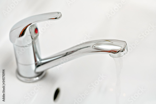 Chrome tap faucet with water flowing, blurred bathroom background